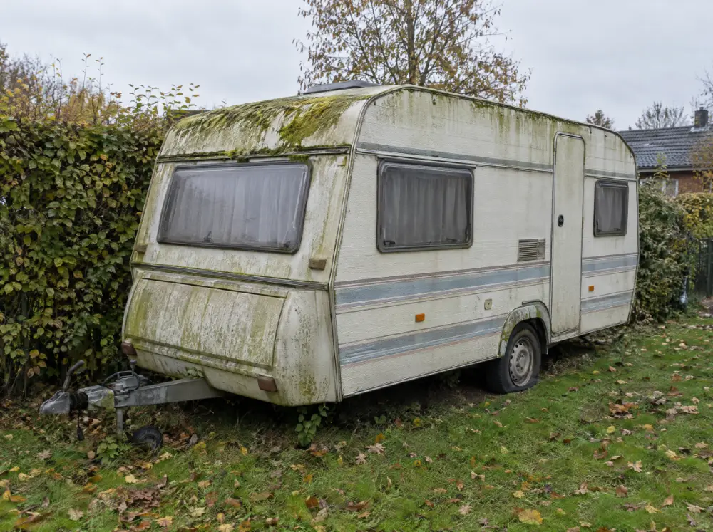Gammel campingvogn med alger på taget i en have